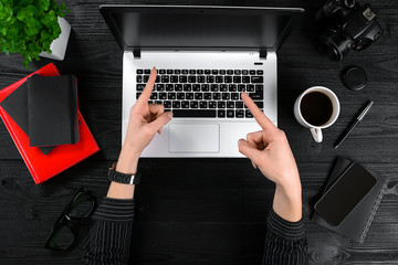 Business and technology topic: the hand of woman in a black shirt showing gesture against background laptop at the desk.