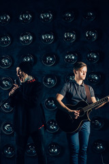 Fototapeta na wymiar two musicians men's light and dark, guitarist, singer, fashionably dressed hipsters on stage, dark background, rock band, jazz, sing a song emotionally