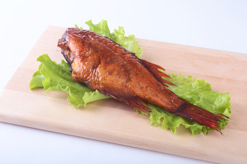 Smoked fish and lemon on green lettuce leaves on Wooden cutting board isolated on white background.