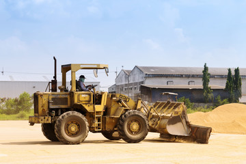 worker is driving a tractor to sweeping paddy rice seeds on the ground after finished drying process outside the rice mill in Ayutthaya, Thailand. agriculture industry.