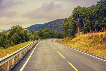 Fototapeta premium Driving a car on the mountain road. Road among mountains with the dramatic stormy cloudy sky. Beautiful nature Norway. 