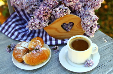 чашка кофе с букетом сирени и круассанами в саду