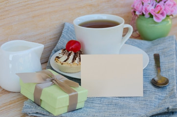 Cup of tea with cute sweet cake, roses and box gift, greeting card with copy space. Woman morning, breakfast surprise concept.