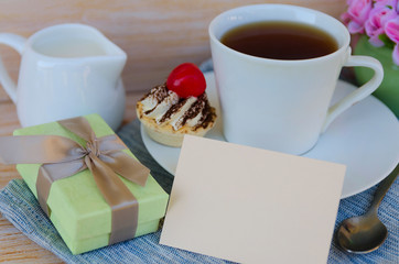 Cup of tea with cute sweet cake, roses and box gift, greeting card with copy space. Woman morning, breakfast surprise concept.