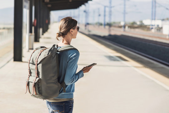 Young woman traveler waiting for a train on a railroad station, travel and active lifestyle concept