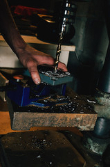 The worker in his garage works on a drilling machine. In the frame, a person's hands