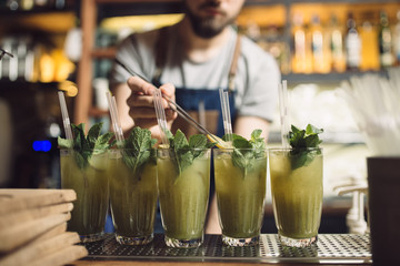 Young male bartender preparing many mochito at a bar counter