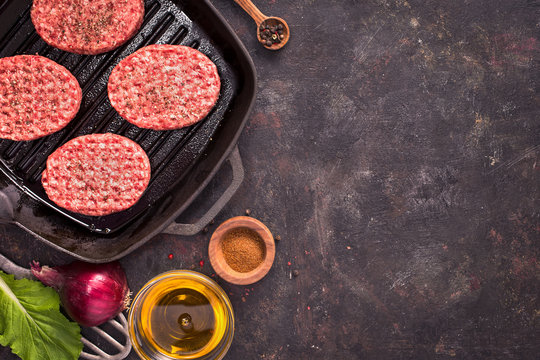 Raw beef meat steak cutlets on grill pan with oil and spices on grunge background top view with copy space