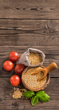 Uncooked quinoa with tomatoes and basil on old wooden background