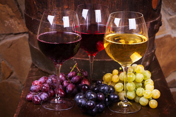 Glasses of red, rose and white wine with cheese, and grape in wine cellar.  Food and drinks concept
