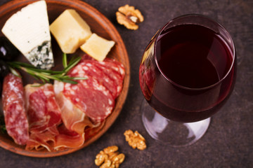 Glass of red wine with cheese, prosciutto and salami. Wine and cheese still life. Food and drinks concept. View from above, top studio shot