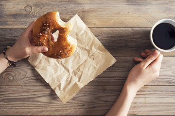 Female hands eating pastry with coffee on wooden table