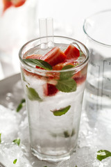 Tasty fresh cold drink with ice, water, mint and strawberry in glass. Closeup.