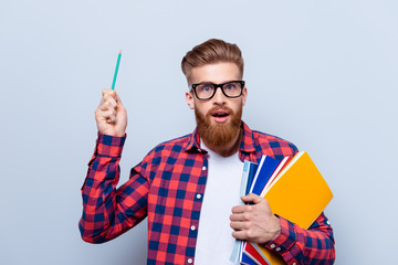 Eureka! Success and science concept. Nerdy young red bearded student standing with books on pure background in glasses and casual outfit with a pencil in hand