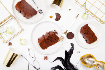 Stylish flat lay with pieces of chocolate cake, white roses, pearl beads. Gold and chocolate concept.