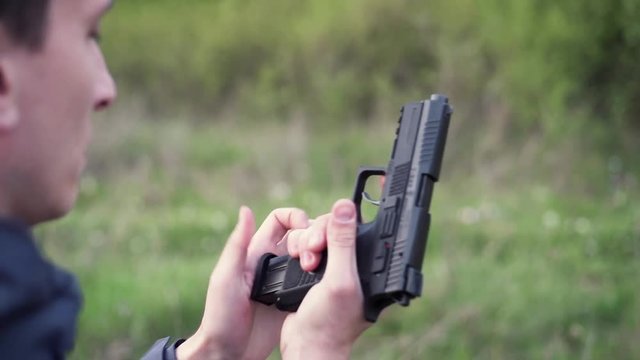 Male hand holding gun, reloading it and shooting from it on a field shooting
