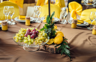 Wedding flower arrangement of yellow roses, greenery and lemons on stump on wedding dinner table, closeup, selective focus