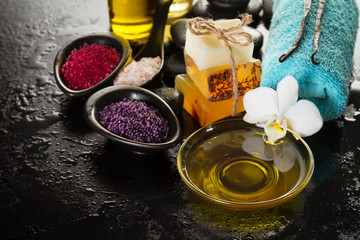 Beautiful Spa Set Spa Products with Essential Oils, Soap, Towel, Spa Sea Salt on Dark Wet Background. Horizontal with Copy Space.