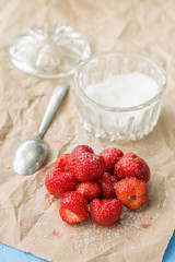 Fresh strawberries with sugar and sugar bowl on the wrinkled brown pack paper