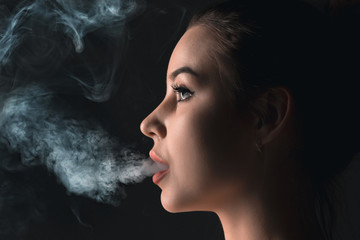 The face of vaping young woman at black studio