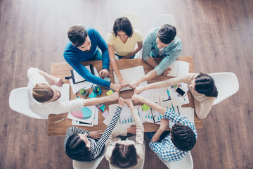 Top up of colleagues putting their fists together in round on top of the table with work stuff in...