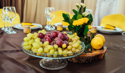 Wedding flower arrangement of yellow roses, greenery and lemons on stump on wedding dinner table, closeup, selective focus
