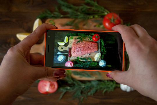 woman hands taking picture of fresh salmon, herbs, spices and vegetables