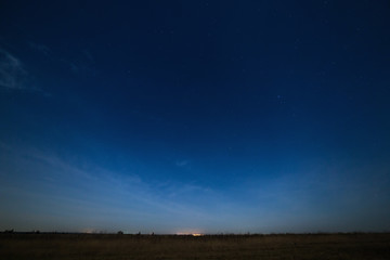 Stars in the night sky with city lights on the horizon. The landscape is photographed by moonlight.