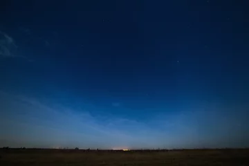 Rolgordijnen Stars in the night sky with city lights on the horizon. The landscape is photographed by moonlight. © olgapkurguzova