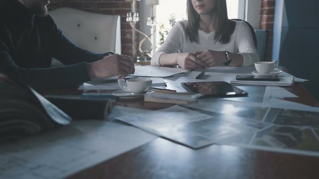 Business meeting with the client: a male designer advises a woman and shows a design project on a tablet. Working meeting: a creative man-designer and a female assistant conduct brainstorming.