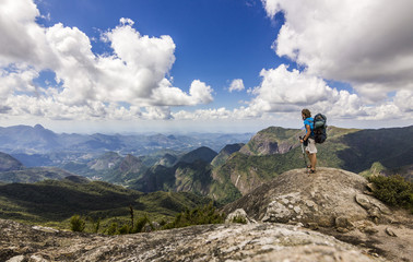 Naklejka premium man with backpack standing on top of mountain with blue sky with clouds