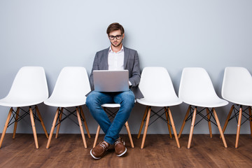 Fototapeta premium Serious confident bearded business man banker in formal wear is typing on his laptop while waiting in the hall on chair