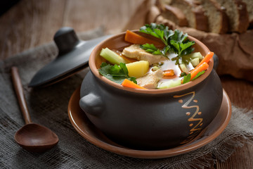 soup in pot, bread, wooden spoon on the table closeup