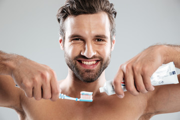 Portrait of a smiling man putting toothpaste on a toothbrush - Powered by Adobe