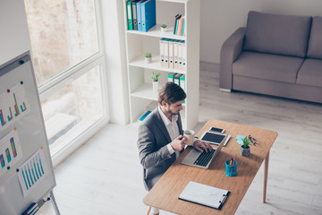 Top view of concentrated young businessman, which is browsing on his laptop at the office and drinking coffee. He is in a suit