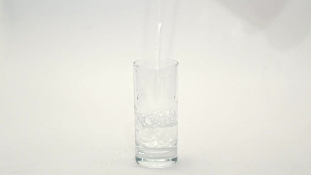 Pour water into a glass on white background. Water poured into glass