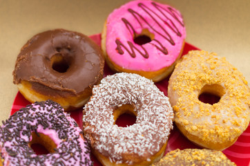 Delicious assorted donuts of different glazed over a red plate in a wooden background