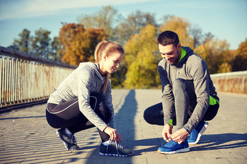 smiling couple tying shoelaces outdoors