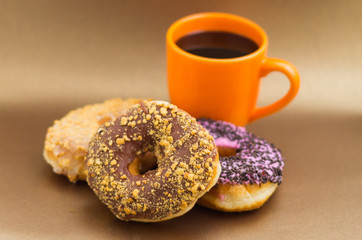 Delicious donuts with chocolate, coconut and pink glazed with some chips of chocolate, with an orange cup of coffee in a wooden background