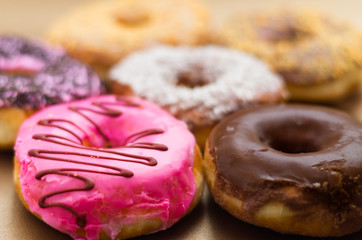 Close up of a delicious assorted donuts of different glazed in a soft brown background