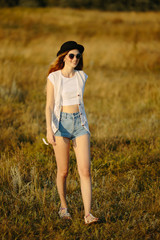 Young pretty woman wearing hat and sunglasses dressed in boho style clothes walking on the nature during beautiful sunset