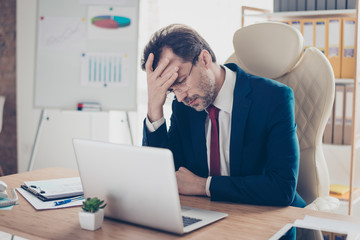 Fototapeta premium Depressed entrepreneur realtor is holding his head with hand, he is tired and frustrated, sitting in the office at his work place