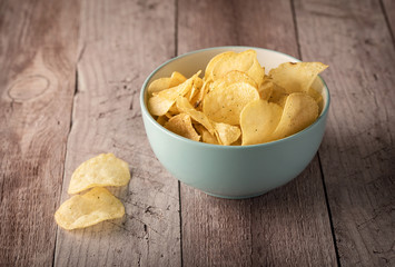 Crispy potato chips in a bowl with milk on wooden