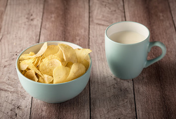 Crispy potato chips in a bowl with milk on wooden