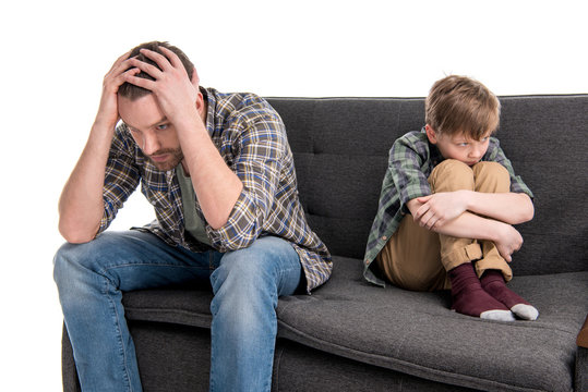 Upset father and son sitting on sofa after quarrel, family problems concept
