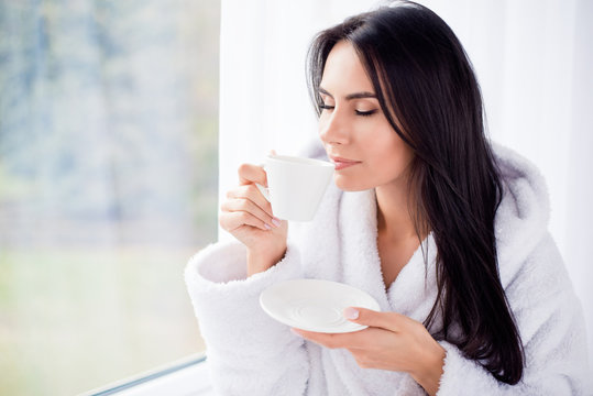 Good morning! Close up portrait of charming dreamy brunette young girl drinking coffee. She is sleepy and relaxed