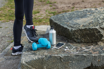A woman in shoes with fitness equipment, headphones and bottle of water on a grass