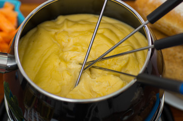 Gourmet Swiss fondue dinner with assorted cheeses and a heated pot of cheese fondue with colorful...