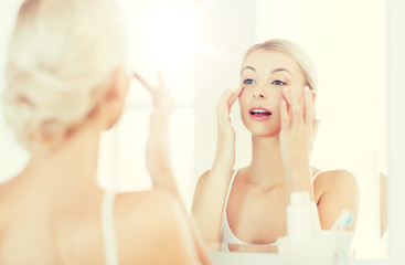 happy woman applying cream to face at bathroom