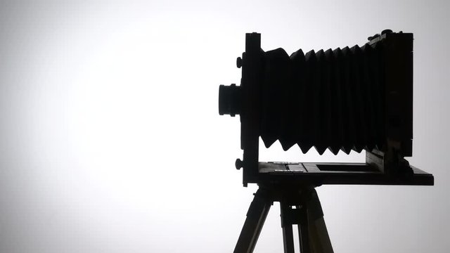 Mid shot shot of old vintage wooden photo camera silhouette slowly spinning the against light in the white background.